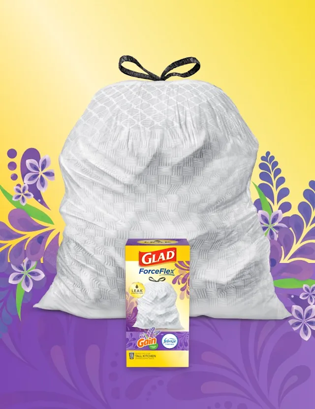 White trashbag with black handles on a background of yellow and purple with lavender illustrations. A box of Glad trash bags sits in front.