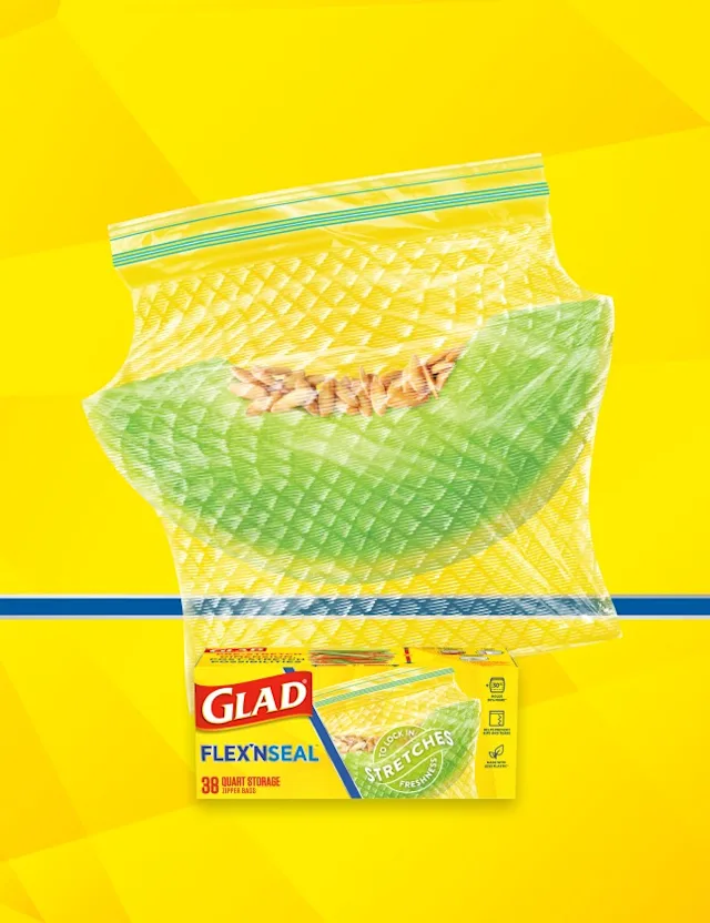 Plastic resealable bag containing a slice of honeydew melon on a yellow background with a blue horizontal line. A box of Glad food storage bags is in the front.