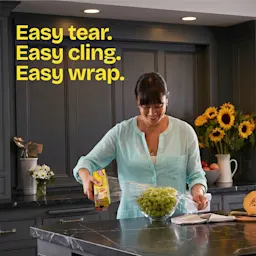 A woman coverin a bowl of grapes with Cling'n Seal in a kitchen. The words "Easy tear. Easy cling. Easy wrap."