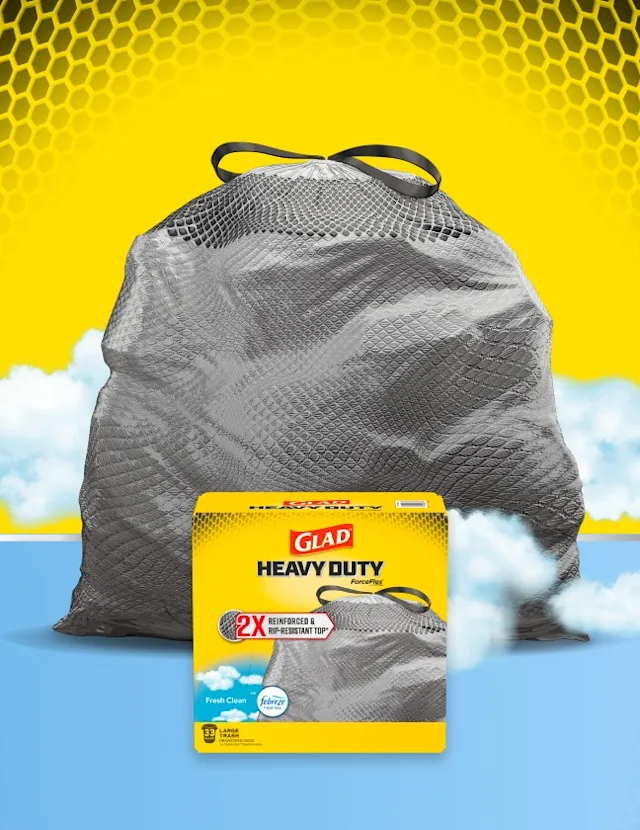 Glad Heavy Duty XL Trash Bag package in front of a gray trash bag, black and yellow and light blue background with clouds