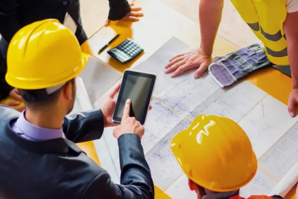 Five employees standing at a desk looking at drawings and pointing at an iPad THUMBNAIL