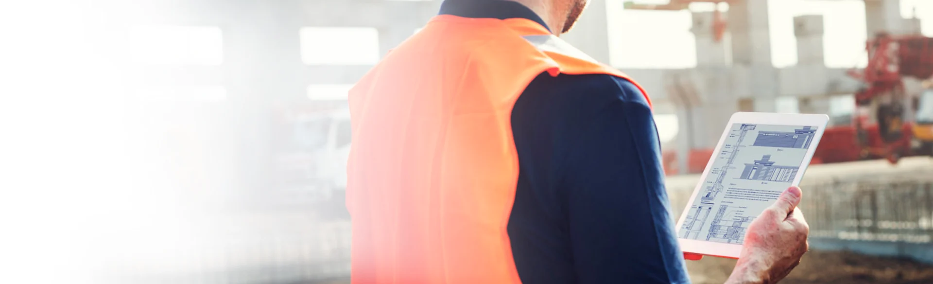 Over the shoulder of construction worker looking at an iPad with drawings 1200x561