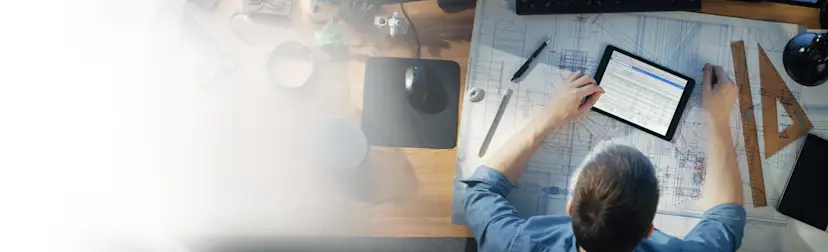 Over head shot of construction worker looking at an iPad and drawings 1200x675