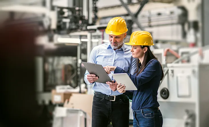 Male and female wearing hard hats on construction site looking at clipboard