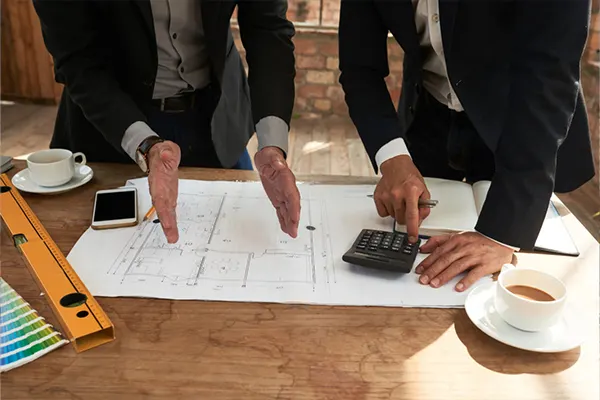 Two executives looking at drawings and using a calculator THUMBNAIL