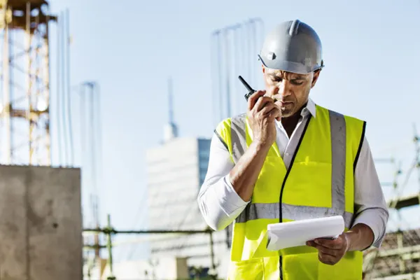 Construction worker on a walkie talkie with a crane in the background THUMB