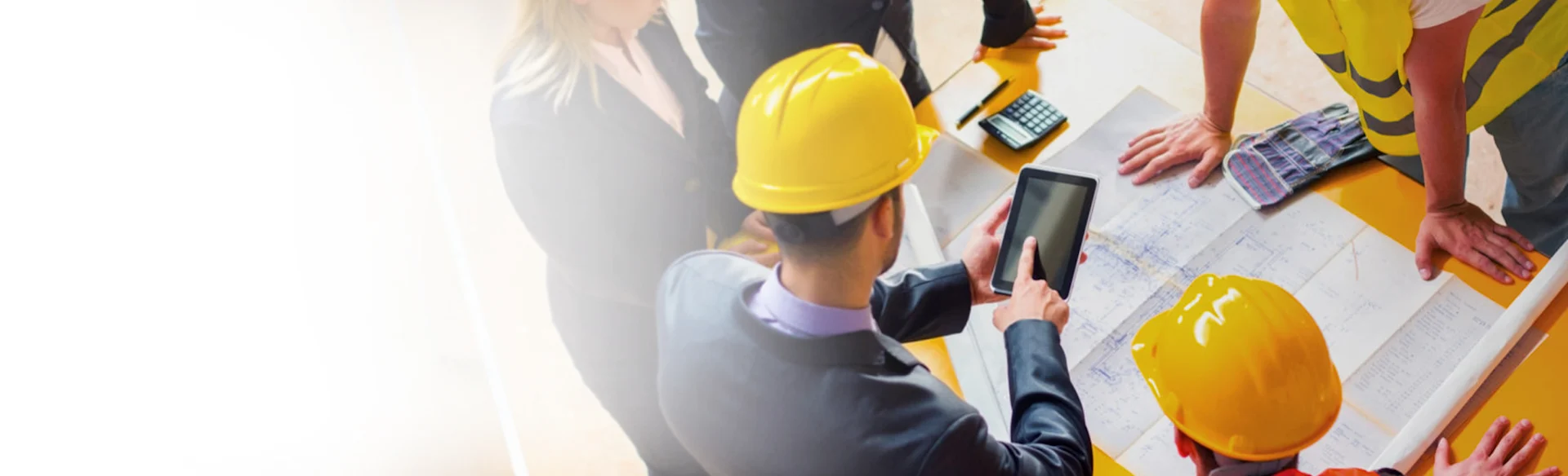 Five employees standing at a desk looking at drawings and pointing at an iPad 1200x543