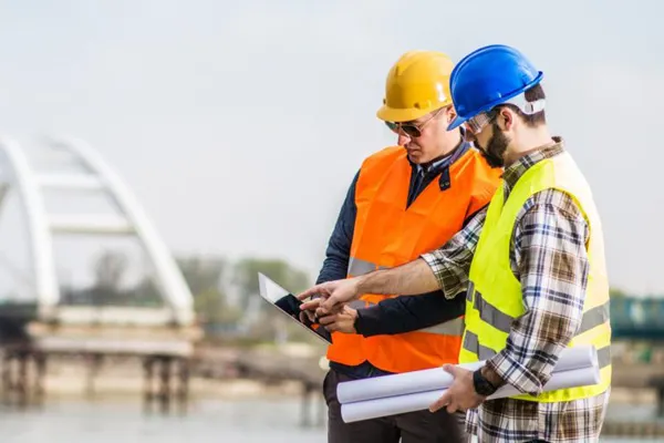 Two construction workers at a work site looking at an iPad 