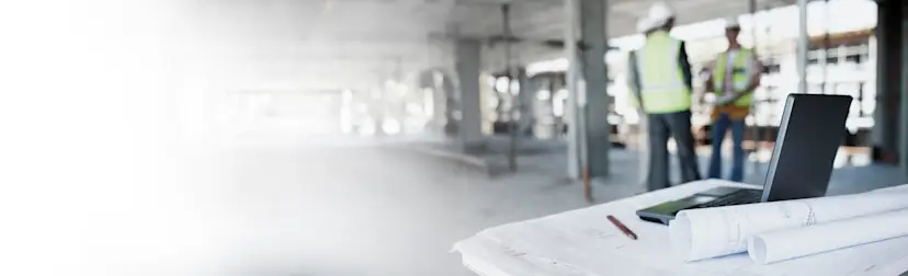 Rolled drawings with three construction workers in the background HERO