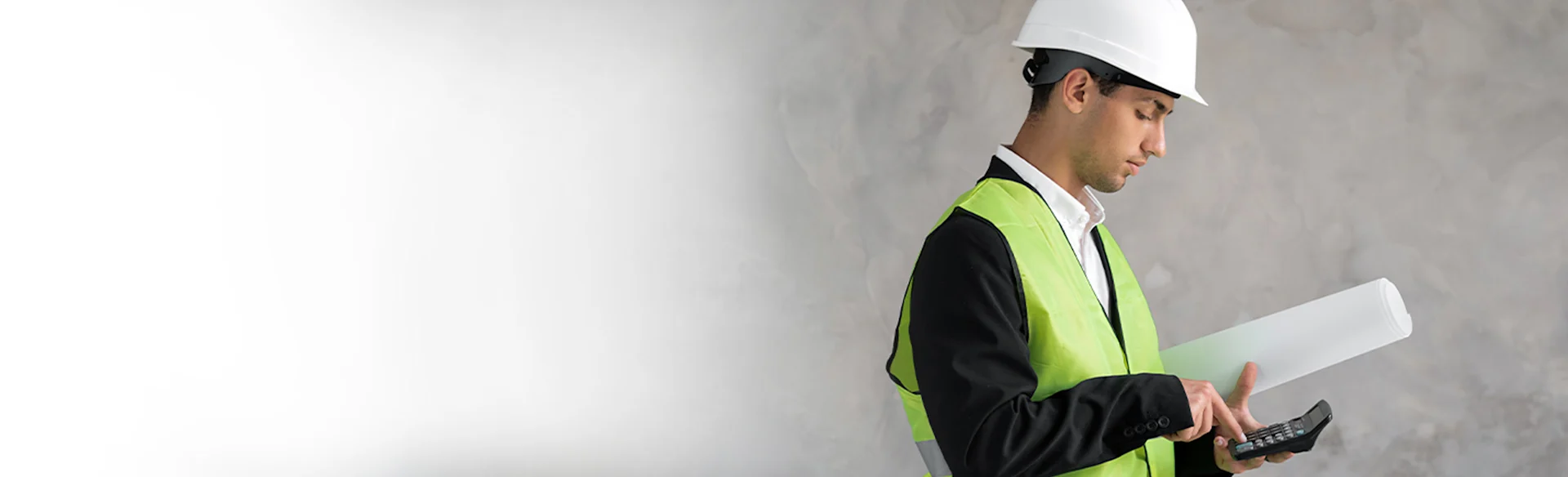 Male construction working holding rolled drawings and using a calculator