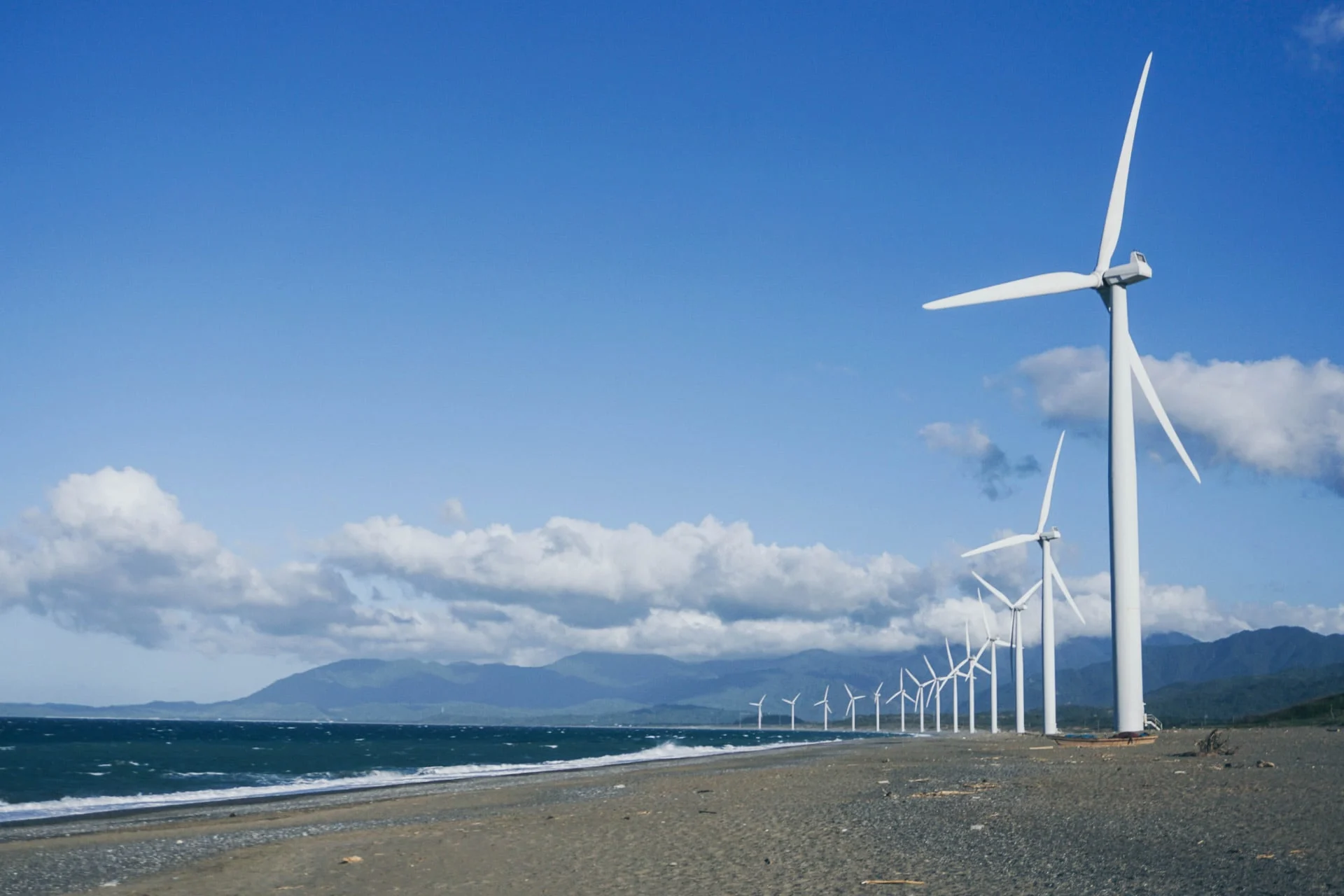 A group of wind turbines on a beach near the ocean.