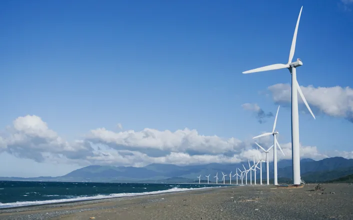 A group of wind turbines on a beach near the ocean.