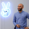 A man standing in front of a neon sign with a peace sign.
