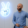 A man standing in front of a neon sign with a peace sign.
