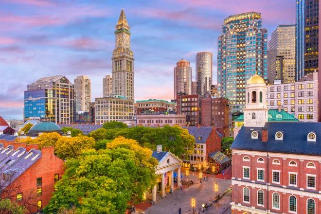 Skyline of boston with historic and modern buildings at dusk, featuring the custom house tower and faneuil hall under a colorful sky.
