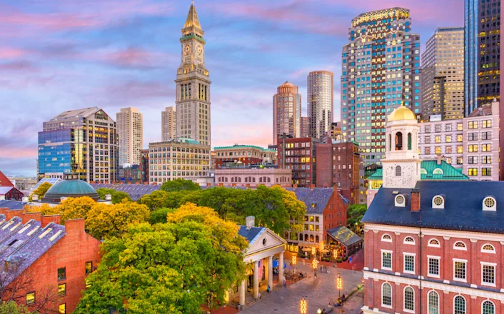 Skyline of boston with historic and modern buildings at dusk, featuring the custom house tower and faneuil hall under a colorful sky.