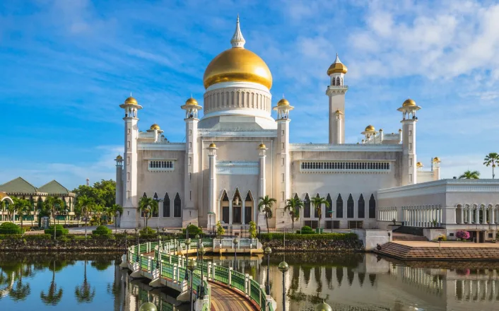 A white mosque with gold domes near a body of water.