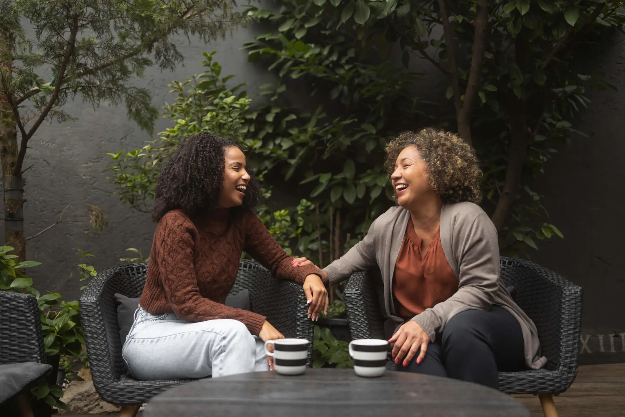 Two black women sitting on chairs in a garden.