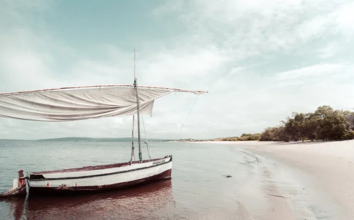 A boat on a beach with a white sail.