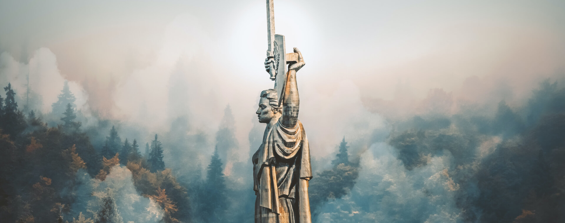 A statue of a man with a sword in the middle of a forest.