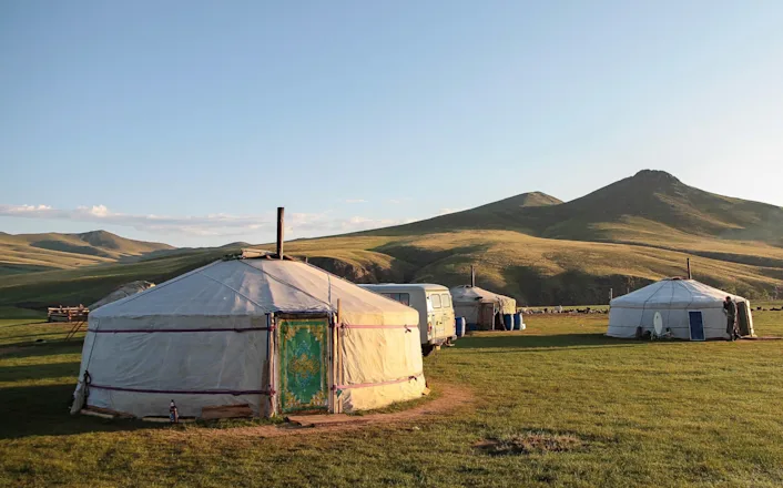 A group of yurts in the middle of a grassy field.