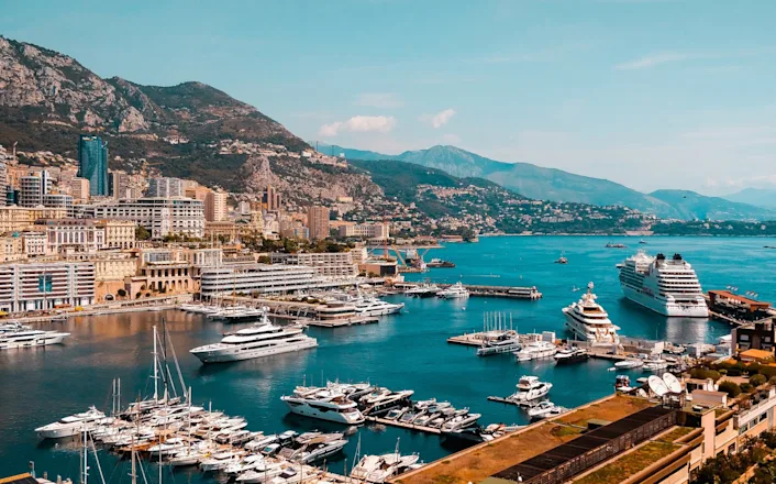 The port of monaco with boats docked and mountains in the background.