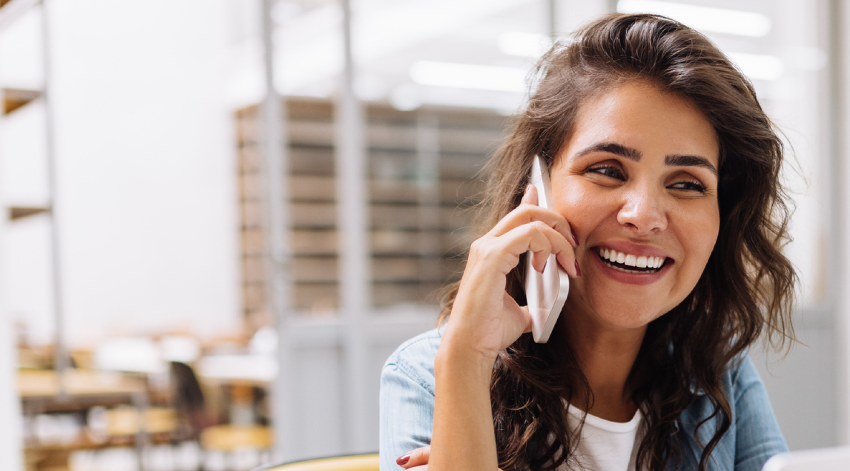 A smiling woman using a cell phone while sitting at a desk.