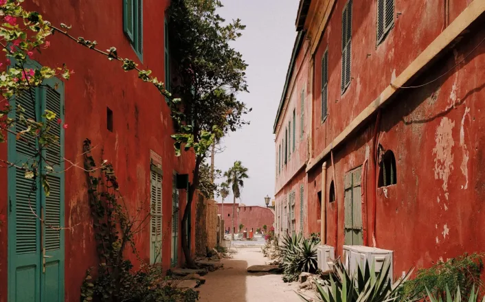 A narrow alley lined with red buildings and plants.