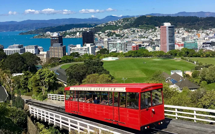 A red trolley is going down a hill with a view of a city.