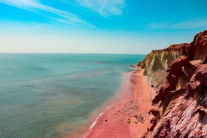 A cliff with red sand and a blue sky.