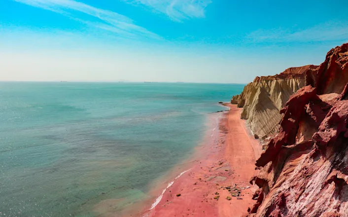 A cliff with red sand and a blue sky.
