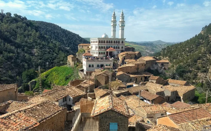 A village in the mountains with a mosque in the background.