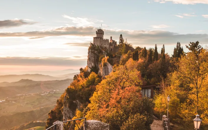 A castle sits on top of a mountain in the fall.