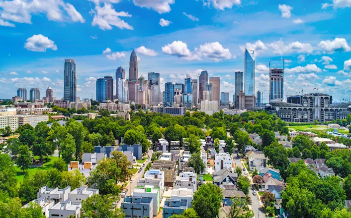Aerial view of a modern city skyline showcasing tall skyscrapers, surrounded by residential areas with greenery, under a blue sky with clouds.