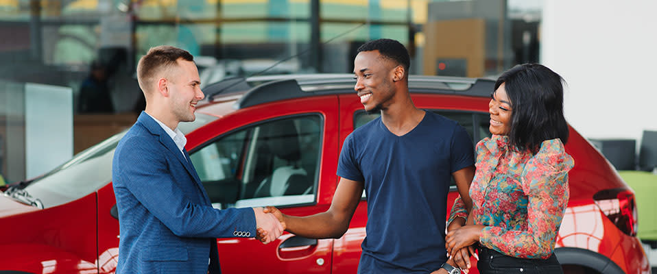 A young African American couple talking to a salesman and buying a car at the car dealership