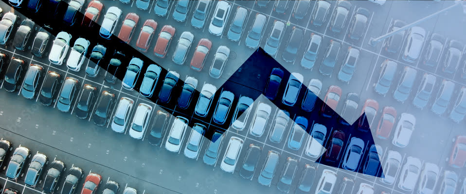 Image of rows of cars in a parking lot overlaid with a jagged arrow representing the economy that is trending down