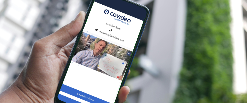 A photo of a person's hand holding a phone with the Covideo logo and some blurred contact information. There is a screenshot of a video on the phone where a man is holding up a whiteboard that says "Hey Covideo Team!"