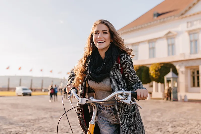 Mulher segurando sua bicicleta e sorrindo enquanto olha para o horizonte.