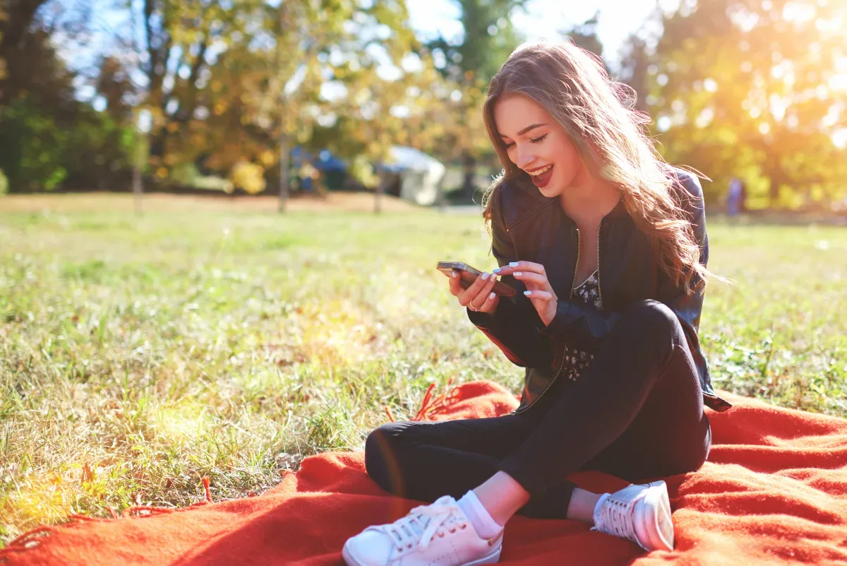 Chica mirando su teléfono mientras está sentada en el césped.