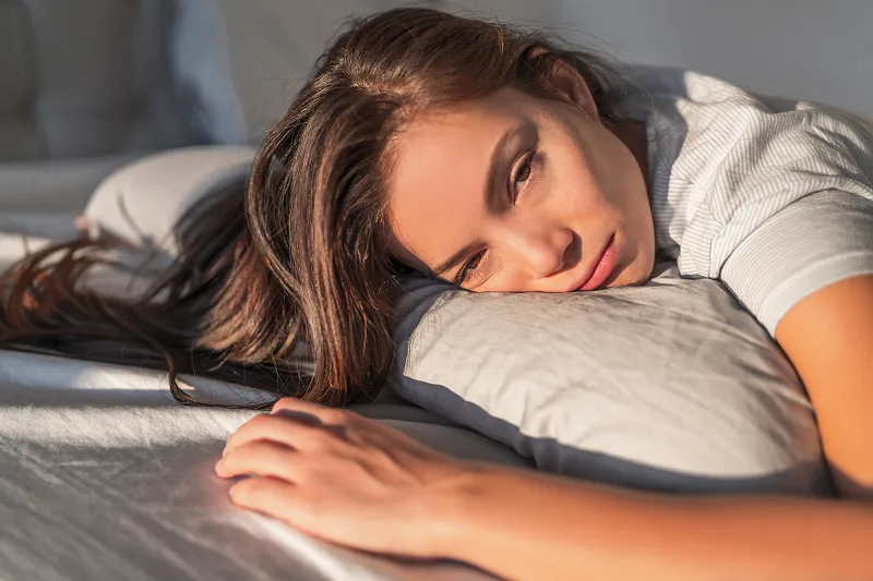 Mulher cansada deitada no sofá, pensando por que se sente cansada antes da menstruação.