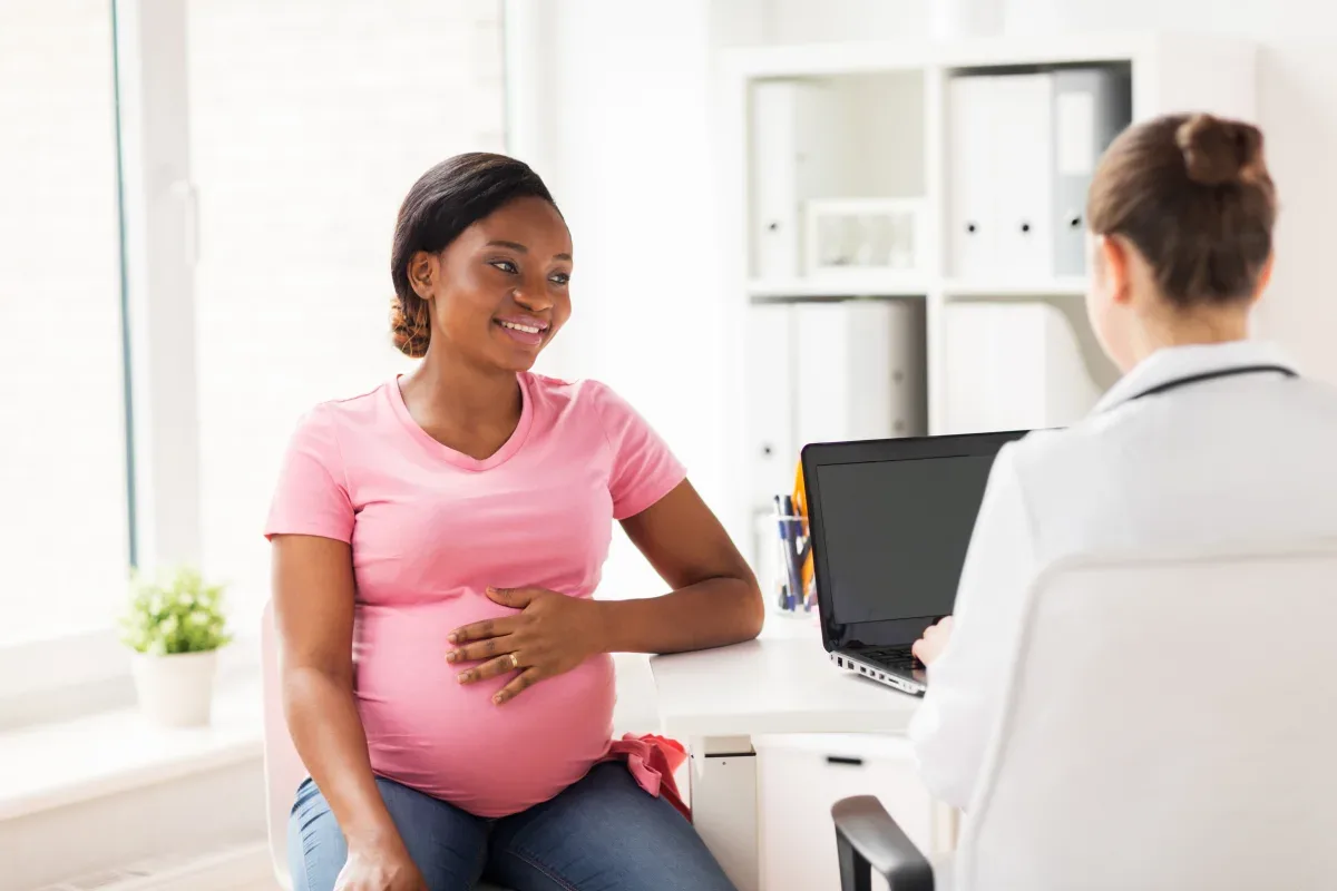 Mulher grávida tocando a barriga e sorrindo no consultório médico.