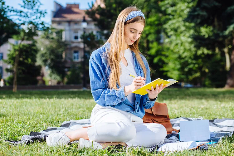 Menina sentada na grama, escrevendo em um caderno.