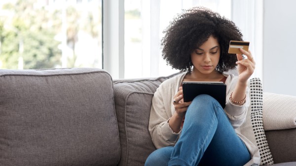 A woman shopping online while sitting on the couch at home.