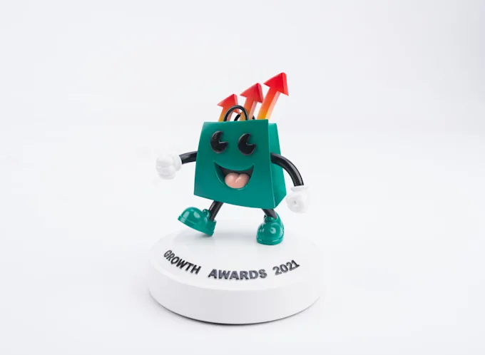 Green shopping-bag mascot figure with arrows on its head standing on a round white award base