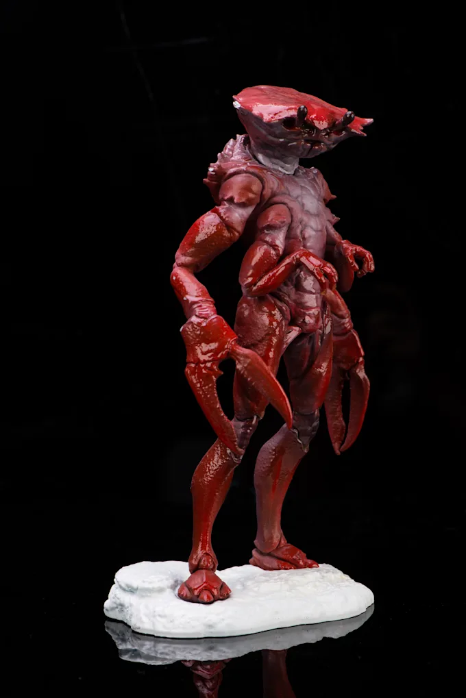 Glossy red creature sculpture with claws on a white base against a black background