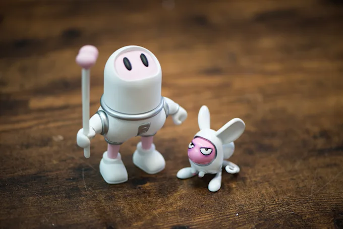 Astronaut character with a staff next to a small white rabbit character on a wooden table