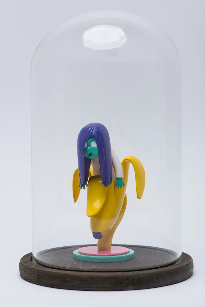 Banana character figure displayed under a glass dome on a wooden base