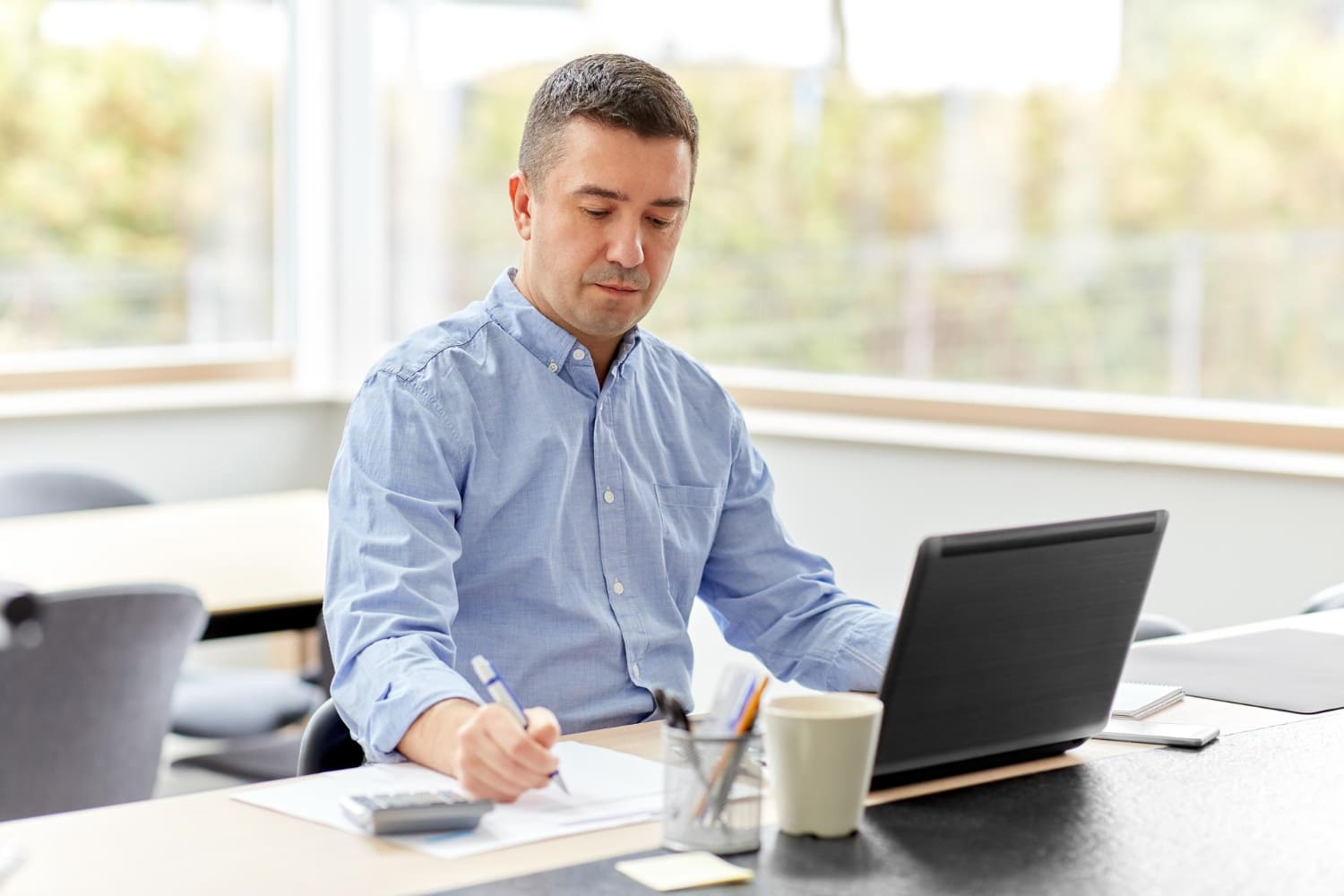 Homem trabalhando concentrando em seu escritório com papéis na mão e em frente ao notebook Homem trabalhando concentrando em seu escritório com papéis na mão e em frente ao notebook