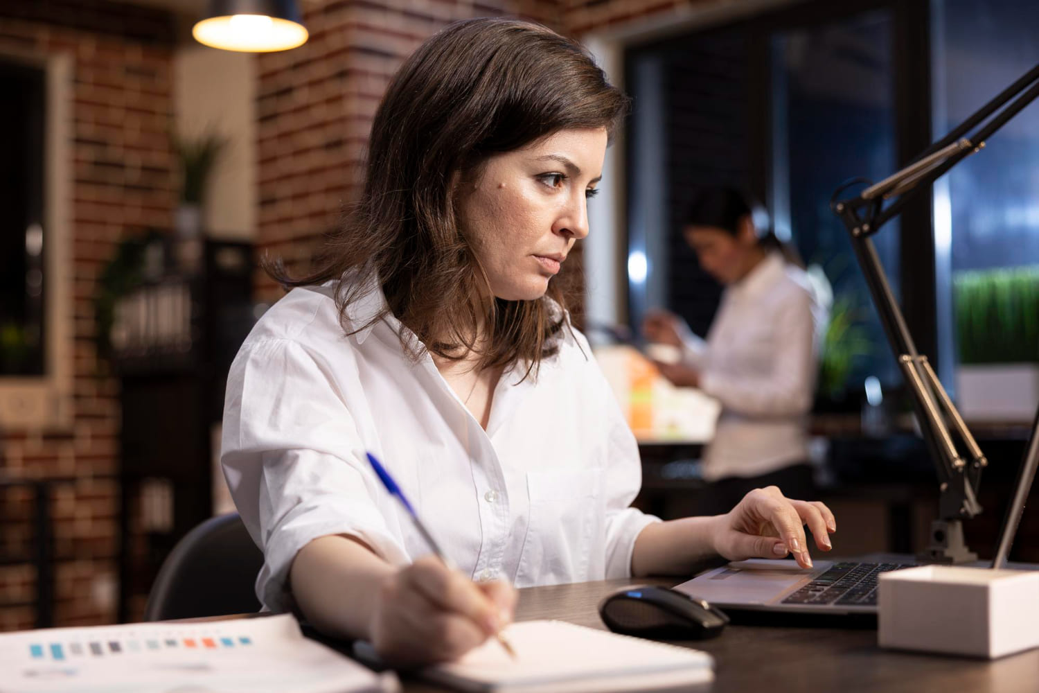 Profissional trabalha em seu escritório usando o notebook e fazendo anotações