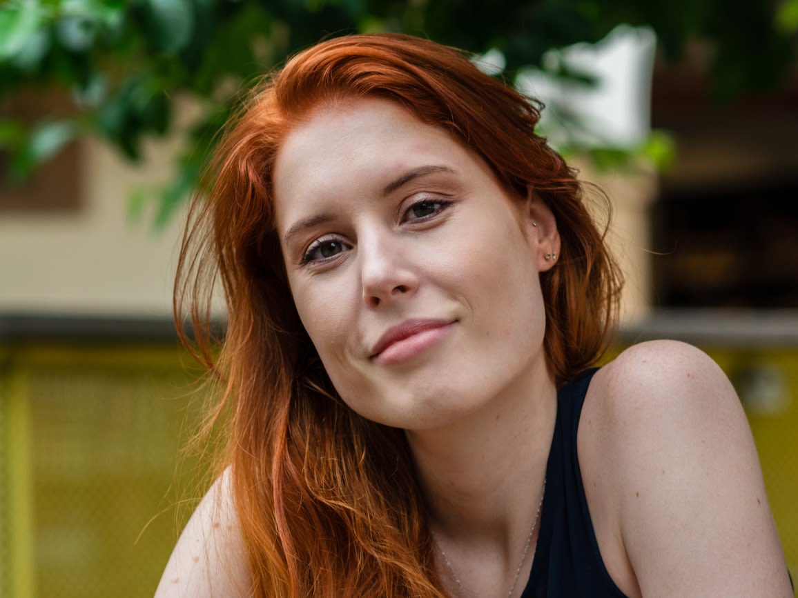 Smiling woman with long red hair and a black vest top.